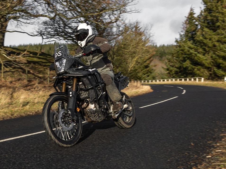 rider with black visor riding black yamaha tenere 700 wr motorcycle around a corner on tarmac road